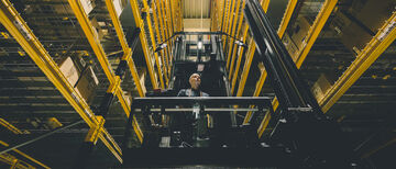 A man on a narrow aisle forklift between two high racks