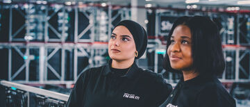 Two employees in Arvato clothing lean casually against a railing and let their gaze wander into the distance