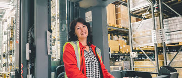 Eine Mitarbeiterin mit Warnweste, die einen Gabelstapler bedient, sieht in die Kamera