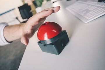 Eine Hand über einem roten Buzzer, kurz davor zu drücken