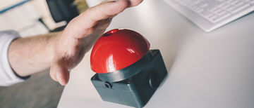 Eine Hand über einem roten Buzzer, kurz davor zu drücken