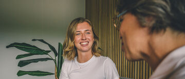 Zwei Mitarbeiterinnen unterhalten sich auf einem Sofa, lächelnde Mitarbeiterin im Fokus